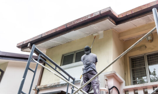 Painter worker adding undercoat foundation paint onto ceiling as primer with roller at residential building.